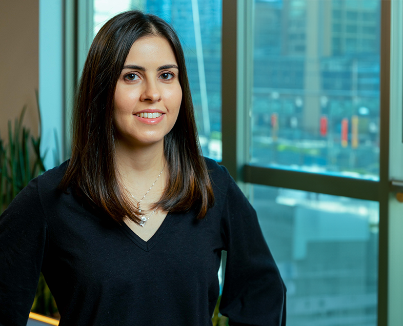 Camila Argentino Silva Ribeiro Scopel  Mulher de cabelo preto na altura dos ombros. Veste uma blusa preta de mangas longas. Ela está em pé, olhando para frente e sorrindo.