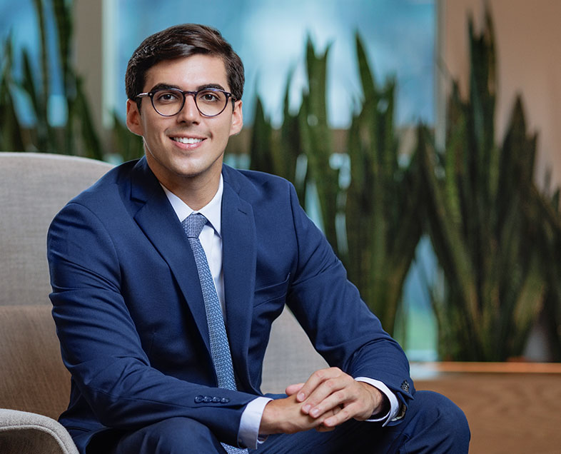 Filipe A. C. Barbalho e Cunha  Homem de cabelo curto preto. Veste uma camisa branca, terno azul escura, gravata azul com estampa quadriculada e usa óculos. Ele está sentado em uma poltrona, virado para a direita, com as mãos entrelaçadas, olhando para frente e sorrindo. 