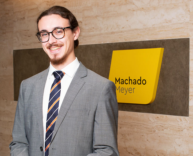 Igor Georg Bechtlufft  Homem de cabelo castanho mediano, com barba mediana e bigode curto da mesma cor. Veste uma camisa branca, terno cinza, gravata azul com faixas laranja na diagonal e usa óculos. Ele está em pé, sorrindo.