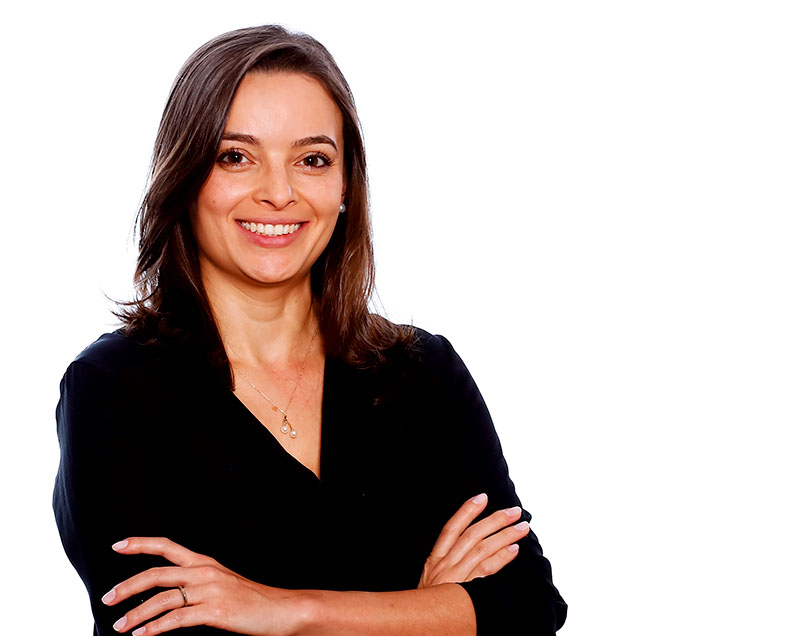 Laura Cavalcante  Mulher de cabelo castanho na altura dos ombros. Veste uma blusa preta de meia manga. Ela está em pé, de braços cruzados, sorrindo.