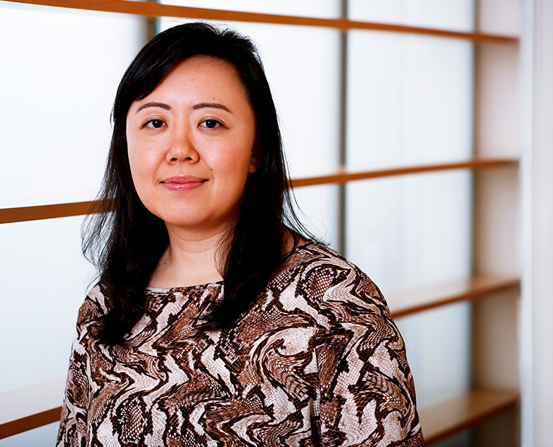 Érica Sumie Yamashita  A woman with shoulder-length black hair. She is wearing an animal print blouse. She is standing, looking straight ahead.