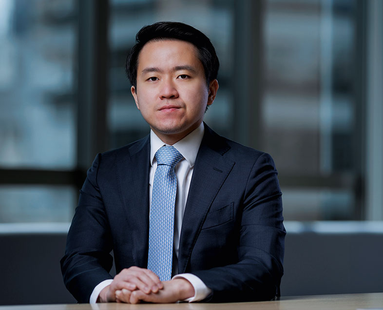 Matheus Wassano Ishigaki  A man with short black hair. He is wearing a white shirt, black suit and blue tie. He is sitting and looking at the photo.