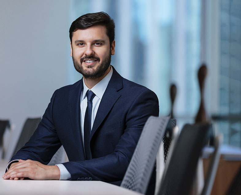 Marcelo de Castro Cunha Filho  A man with short black hair. He is wearing a white shirt, black suit and black tie. He is sitting on a chair, his hands intertwined and resting on a table in front of him, smiling.