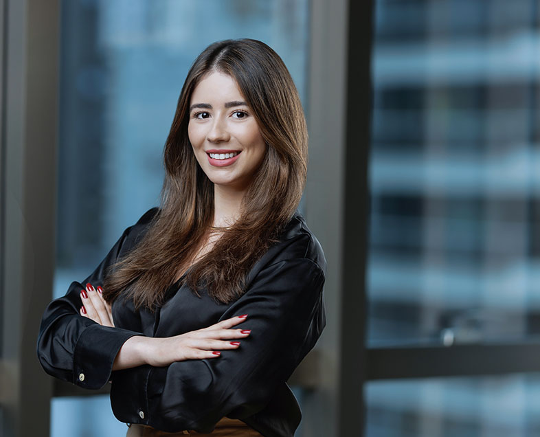 Nathália Ohana Freitas da Silva  Mulher de cabelo castanho comprido. Veste uma blusa preta de mangas longas bufantes. Ela está em pé, virada para a esquerda, com os braços cruzados, olhando para frente e sorrindo.