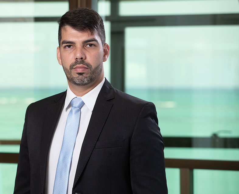 Renato Carvalho Barbosa de Lima  Homem de cabelo preto curto com barba e bigode curtos da mesma cor. Veste uma camisa branca, terno preto e gravata azul. Ele está em pé, olhando para frente e sorrindo.