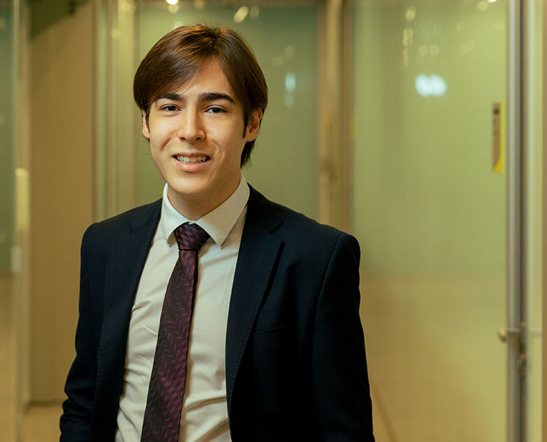 Rafael Costa Silva  Homem de cabelo castanho mediano. Veste uma camisa branca, terno preto e gravata preta. Ele está em pé, olhando para frente e sorrindo.