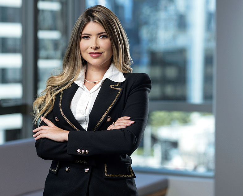 Thaís Helena Valente Teixeira Lima  Mulher de cabelo castanho comprido e ondulado, com as pontas loiras. Veste uma blusa branca, um blazer preto e uma saia  curta preta. Ela está em pé, de braços cruzados, olhando para frente e sorrindo.