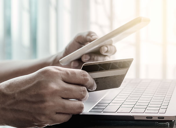 Person holding a credit card in one hand while typing on a cell phone with the other. In the background, a silver notebook is positioned above a table