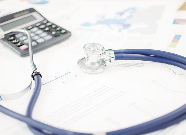 A stethoscope with a blue cord and silver ends is positioned above various scattered papers. In the background, a gray calculator with black and light gray buttons.