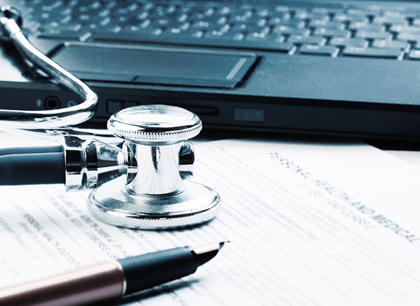 Stethoscope positioned above white A4 sheet of paper. Open black notebook in the background