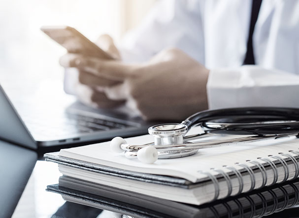 Stethoscope above a notebook with blank pages. In the background, a person is typing on a cell phone while sitting down