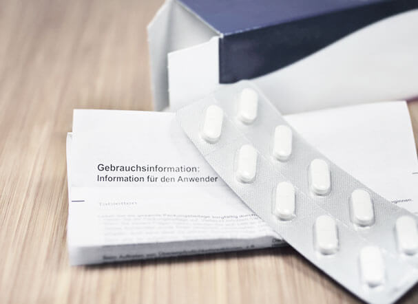 Carton of medicines in white, positioned above a leaflet. In the background, a navy blue pill box